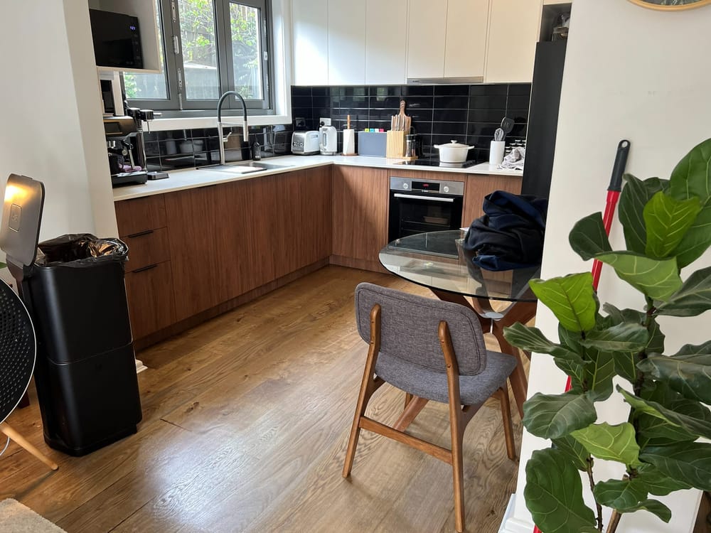 The finished kitchen seen from the dining area, with timber-look fronts and a black tiled splashback